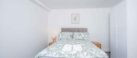 Une chambre à coucher comprenant un lit, des tables de chevet, une commode, une lampe, une armoire et un tableau encadré accroché au mur.