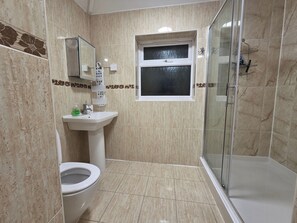 Et badeværelse med toilet, vask og glasvæg omkring bruseren.