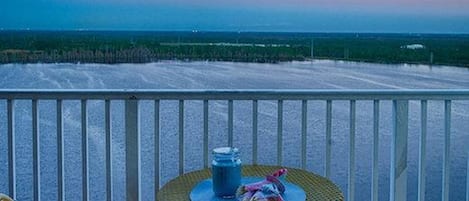 A balcony with two wicker chairs and a small round table, overlooking a beach and ocean.