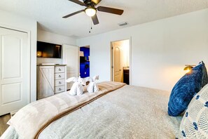 Ein Schlafzimmer mit einem Bett, Kissen, einem Deckenventilator, einer Kommode und einem Fernseher.