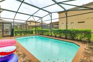 Ein Schwimmbecken mit Glasüberdachung, umgeben von einer Ziegelterrasse und Grünflächen.