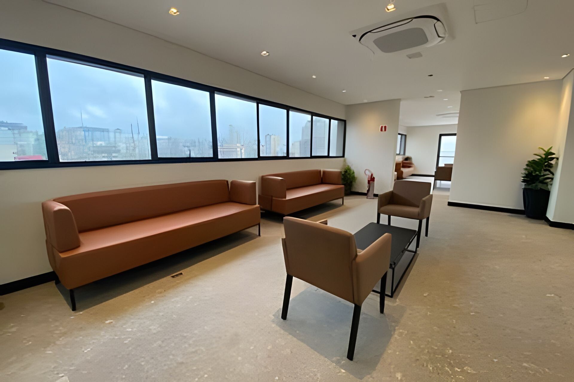 Un salón amplio con un sofá grande, una mesita y dos sillones. Ventanas amplias ofrecen vistas de la ciudad.
