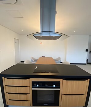 A modern kitchen with a central island, built-in oven, and a stainless steel range hood. - SHB Studio incrível a 3 min da Paulista (São Paulo)