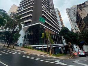 Un edificio moderno con fachada de vidrio, varios pisos y un letrero verde que indica un espacio de negocios u oficina.