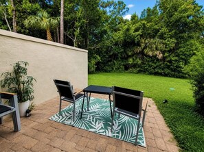 An outdoor patio with a table and chairs, a potted plant, and a grassy lawn. - Modern Champions Gate Retreat - 2 Primary Suites - 5 Beds - Sleeps 10 (Davenport)