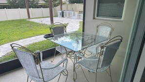A glass-top table with four wicker chairs, a black lamp, and a view of a grassy yard and a white fence. - House for rent, 12 minutes from Orlando Airport and 25 minutes from the parks. (Orlando)