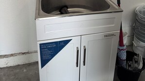A compact all-in-one laundry sink cabinet with a stainless steel sink, a faucet, and a soap dispenser. - House for rent, 12 minutes from Orlando Airport and 25 minutes from the parks. (Orlando)