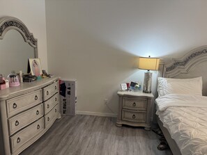 Ein Schlafzimmer mit einem Bett, einem Nachttisch mit Lampe, einer Kommode mit Schubladen und einem Spiegel.