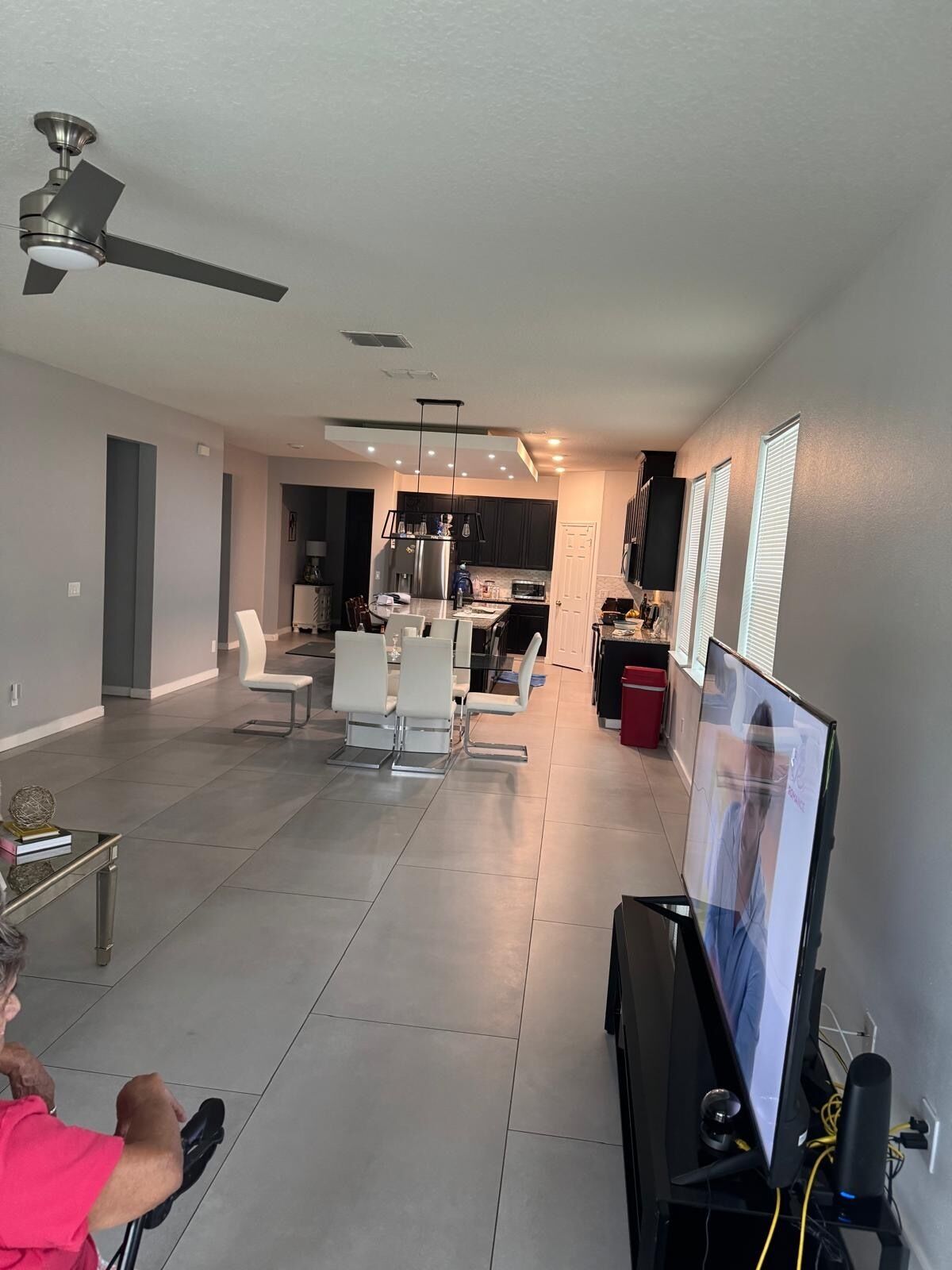 A modern living room with a flat-screen TV, a ceiling fan, and a dining area with white chairs.