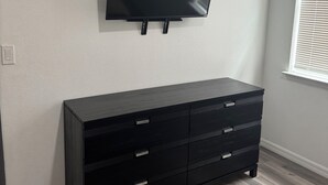 A room with a flat-screen TV mounted on the wall, a dark wooden dresser with drawers, and a window with blinds. - House for rent, 12 minutes from Orlando Airport and 25 minutes from the parks. (Orlando)