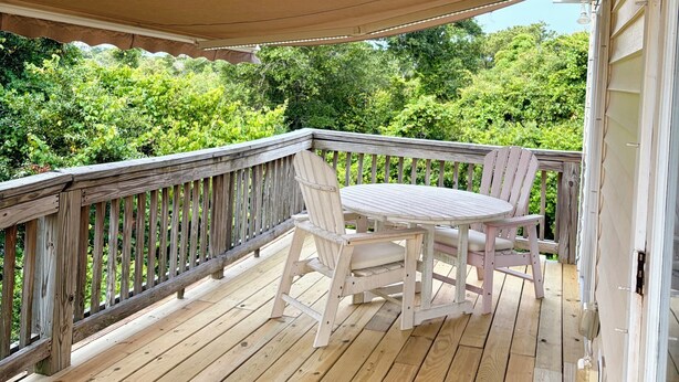 Une terrasse en bois avec une table et des chaises, une rambarde et un espace abrité.