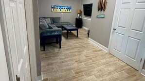 Une pièce avec un canapé gris, une table basse, un téléviseur et une porte sur laquelle est apposée une pancarte.