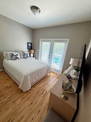 A bedroom with a bed, a desk with a lamp, a television, and a window with blinds. - Where Isle Be•Relax & Unwind• 4 bed• 4 bath• Sleeps 8 (Emerald Isle)