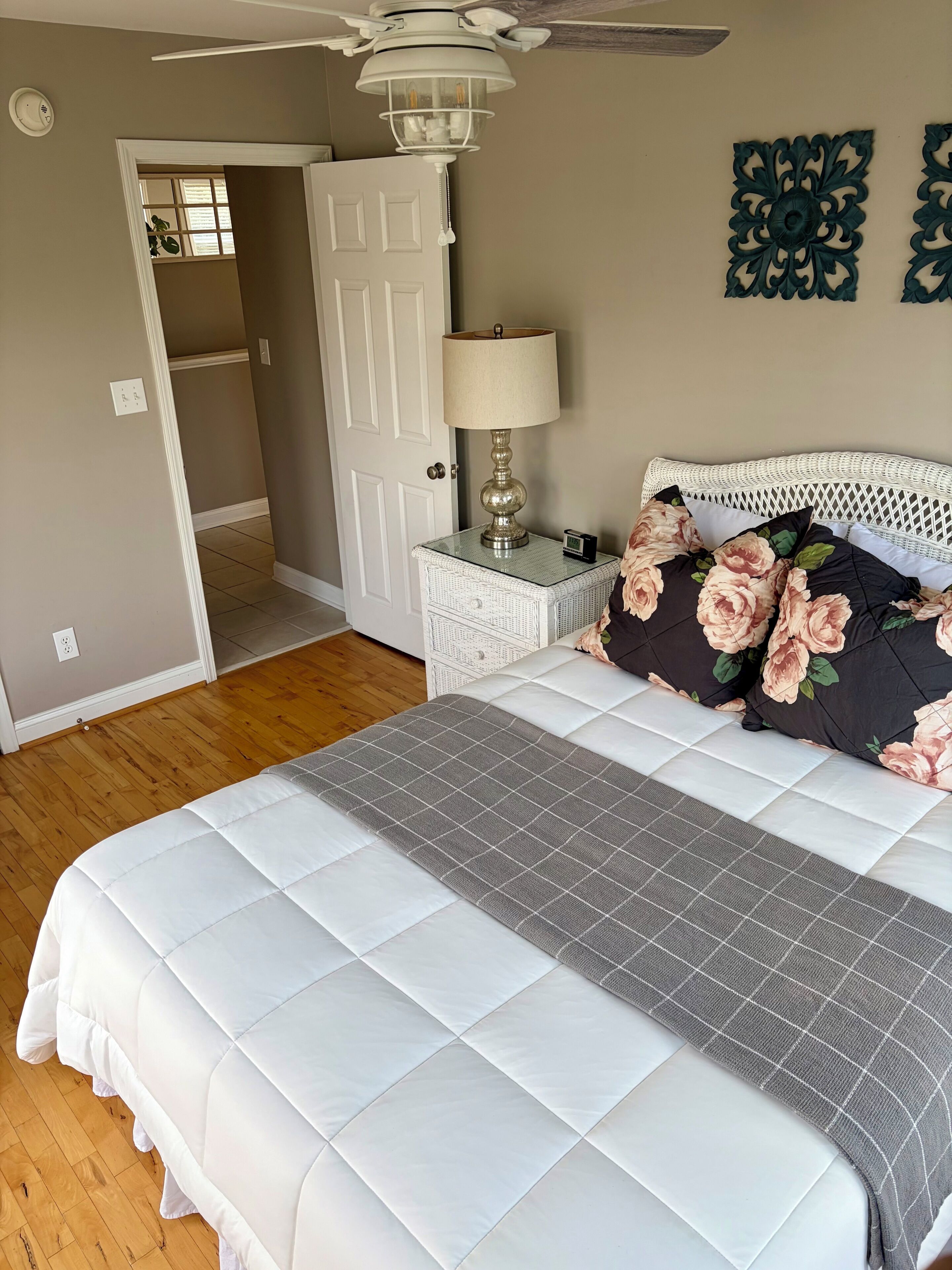 A bedroom with a bed, a nightstand, a lamp, a ceiling fan, a door, and a wall decoration.