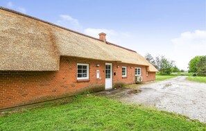 Ein Backsteinhaus mit Strohdach, einer Schotterauffahrt und einer Rasenfläche.