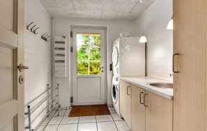 Ein kleiner Waschraum mit Tür, Fenster, Waschmaschine, Trockner, Spüle und einem Metallregal.