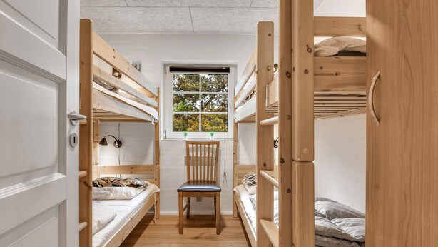 Habitación tipo dormitorio con literas, un escritorio, una silla y una ventana con vista a árboles.