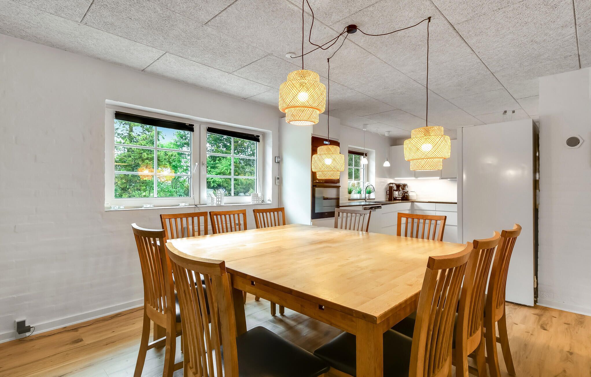 Comedor con mesa y sillas de madera, ventanas amplias y lámparas colgantes de mimbre.
