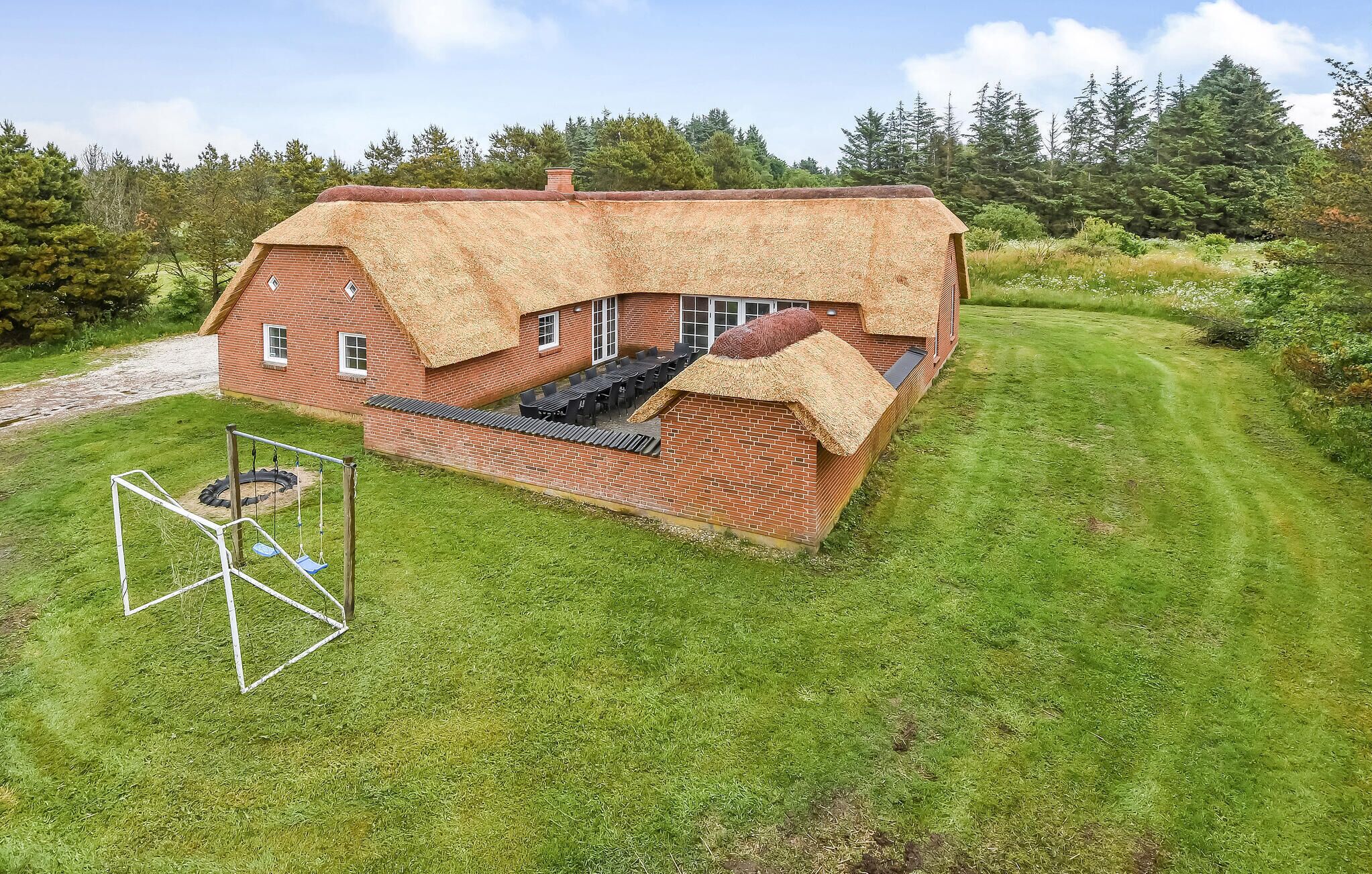 A house with a thatched roof, brick walls, and a swing set in the yard.