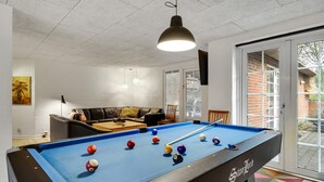 Una mesa de billar con bolas, un sofá y una puerta que da al exterior.