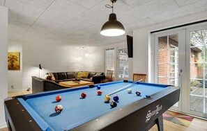 Ein Billardtisch mit Kugeln, eine Couch und eine Tür, die nach draußen führt.