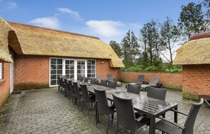 Ein Gebäude aus Ziegeln mit einem Reetdach, einer Terrasse mit Tisch und Stühlen und einer Ziegelmauer.