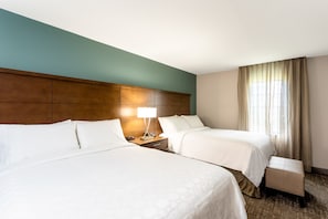 Camera d'albergo con due letti, un comodino con una lampada, una testiera in legno e una finestra con tende.