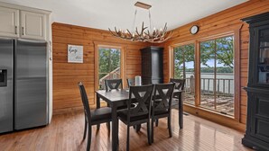 Eine Küche mit Holzwänden, einem Edelstahlkühlschrank, einem Esstisch mit Stühlen und Seeblick durch große Fenster.