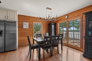 Eine Küche mit Holzwänden, einem Edelstahlkühlschrank, einem Esstisch mit Stühlen und Seeblick durch große Fenster.