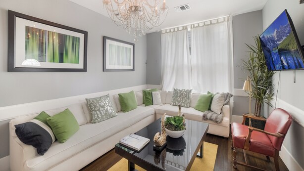 A modern living room with a white sofa, green and white pillows, a black coffee table, a red leather chair, a chandelier, and a framed picture on the wall. - Downtown Mansion 10 bedrooms/7.5 baths, 34+ people, 11car gated parking, Jacuzzi (San Antonio)