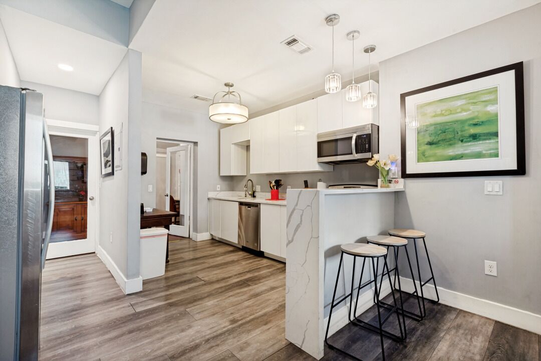 Una cocina moderna con armarios blancos, un microondas y una zona de bar con taburetes.