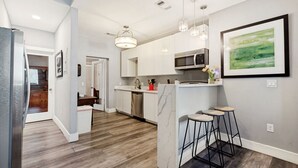 A modern kitchen with white cabinets, a microwave, and a bar area with stools. - Downtown Mansion 10 bedrooms/7.5 baths, 34+ people, 11car gated parking, Jacuzzi (San Antonio)