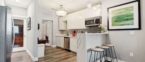 Una cocina moderna con armarios blancos, un microondas y una zona de bar con taburetes.
