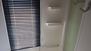 Ein schmaler Flur mit einem Fenster mit Jalousien, einem weißen Heizkörper und einer Tür mit Kleiderhaken.