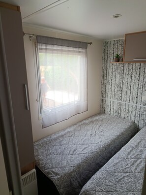 A room with a bed, a window with sheer curtains, a radiator, and a wall with a patterned wallpaper. - Mobile home 50 meters from the beach Natural surroundings Family vacations (Agde)