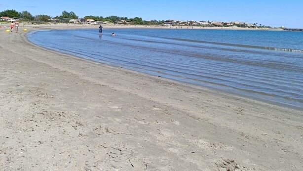 Ein Strand mit blauem Himmel, ruhigem Wasser und einigen Personen.