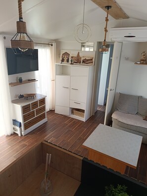 Een moderne woonkamer met een flatscreen televisie, houten vloeren, een bank en een eethoek.