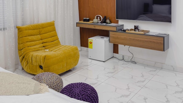Ein modernes Schlafzimmer mit gelbem Sessel, Bett, Fernseher und einem kleinen weißen Gerät.