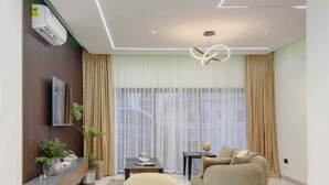 Ein modernes Wohnzimmer mit einer Couch, einem Fernseher, einem Esstisch mit Stühlen und einem großen Fenster mit Vorhängen.