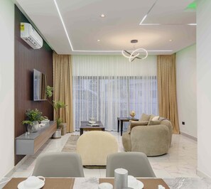 A modern living room with a sofa, a TV, a dining table with chairs, and a large window with curtains. - Veranda suite a spacious cozy 1 bedroom (Accra)