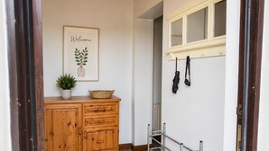 Ein Flur mit einem Holzschrank, einem Willkommensschild, einem Schuhregal und einer schwarzen Matte.