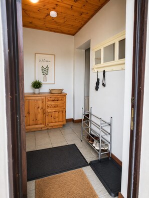 Ein Flur mit einem Holzschrank, einem Willkommensschild, einem Schuhregal und einer schwarzen Matte.
