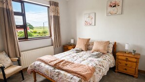 Ein Schlafzimmer mit einem Bett, zwei Nachttischen, einem Sessel, einem Fenster mit Vorhängen und einer Heizung.