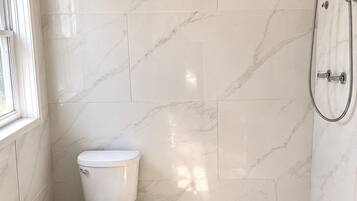 Un baño con inodoro, ducha con cabezal de ducha manual y ventana.