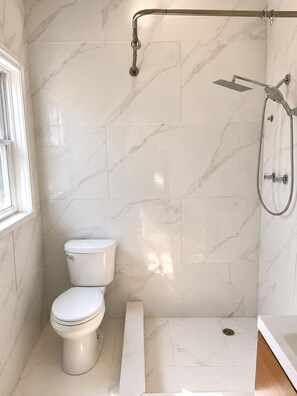 Ein Badezimmer mit Toilette, einer Dusche inklusive Duschbrause und einem Fenster.