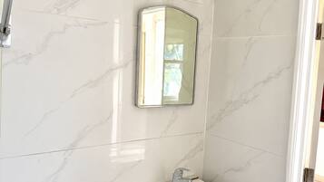 Un baño con ducha, lavamanos y espejo.