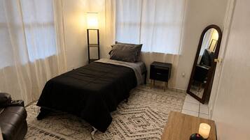 Un dormitorio con cama, mesita de noche, lámpara, espejo y una pequeña mesa de madera con una vela.