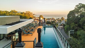 A rooftop pool with lounge chairs, a view of the city, and a road with cars. - Studio Saint Garden - Sunset - Swimming pool with ocean view - Gastronomy (Florianópolis)