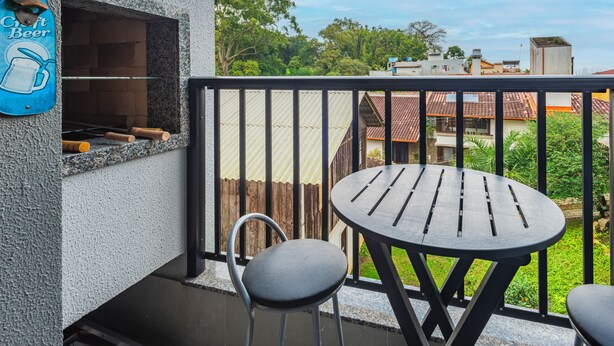 A balcony with a grill, a table, and two chairs. - Studio Saint Garden - Sunset - Swimming pool with ocean view - Gastronomy (Florianópolis)