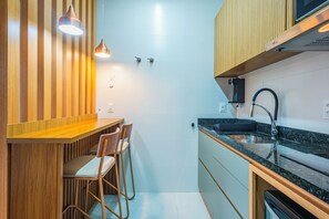 A compact kitchen with a wooden bar counter, two bar stools, a sink, and a dishwasher. - Studio Saint Garden - Sunset - Swimming pool with ocean view - Gastronomy (Florianópolis)